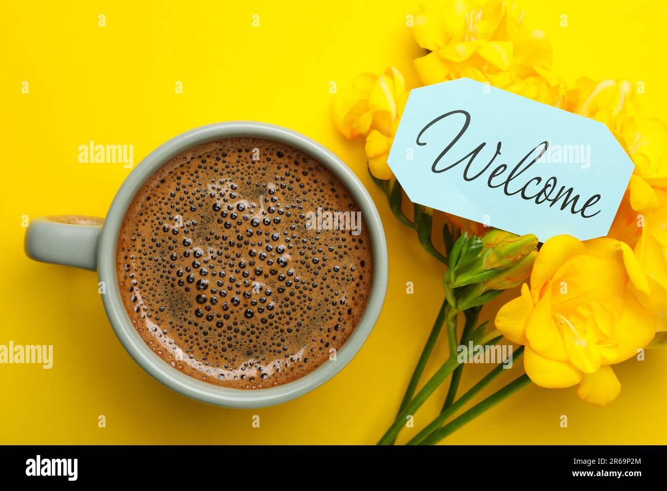 Carte de bienvenue, belles fleurs de freesia et une tasse de café aromatique sur fond jaune, plat Banque D'Images