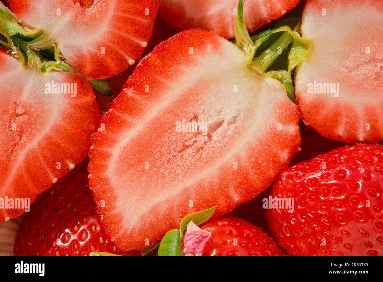 La moitié d'une fraise en gros plan sur une table en bois, récolte saisonnière de baies, vue de dessus, idée d'un fond de fraise ou de faire des desserts Banque D'Images