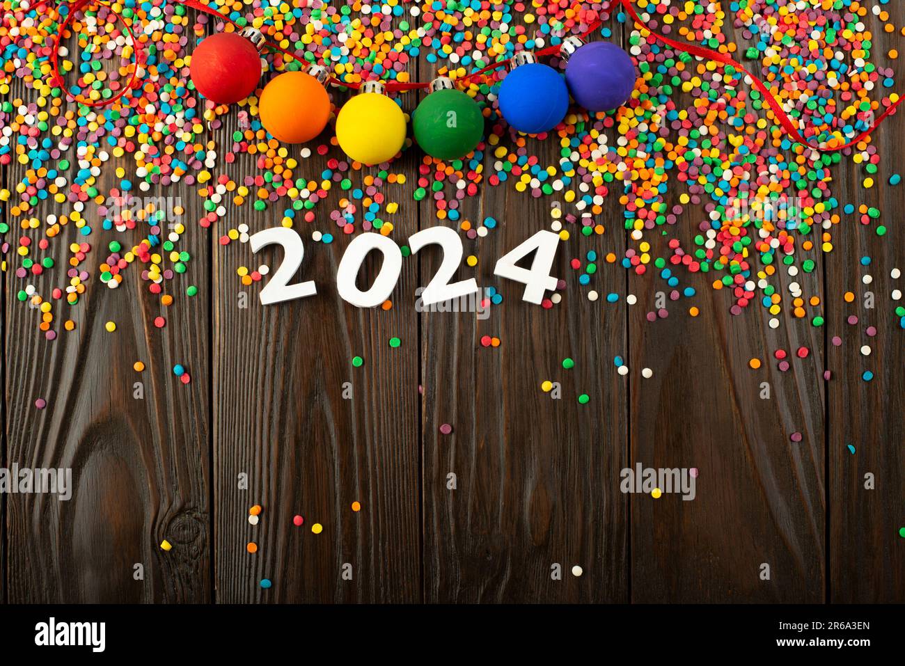 Les numéros blancs 2024 et les sucreries de couleur sur une table en bois avec guirlande de boules de couleur Banque D'Images