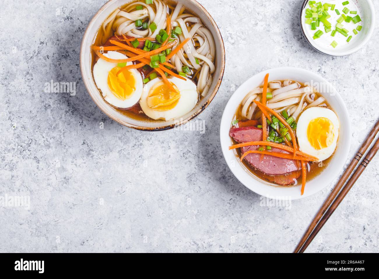 Bols avec ramen de soupe japonais, baguettes, fond rustique en béton blanc. Soupe asiatique traditionnelle avec nouilles, viande, bouillon, œufs. Cuisine asiatique. Banque D'Images