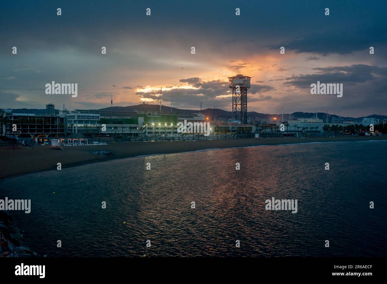 La promenade maritime et la plage de la Barceloneta au coucher du soleil avec la tour de treillis Torre Sant Sebastià abritant également le restaurant Torre de Alta Mar. Banque D'Images