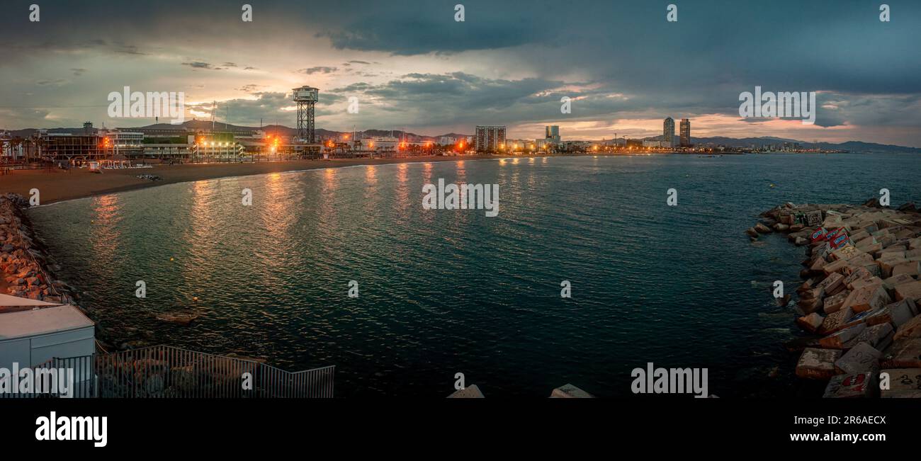 La promenade maritime et la plage de la Barceloneta au coucher du soleil avec la tour de treillis Torre Sant Sebastià abritant également le restaurant Torre de Alta Mar. Banque D'Images