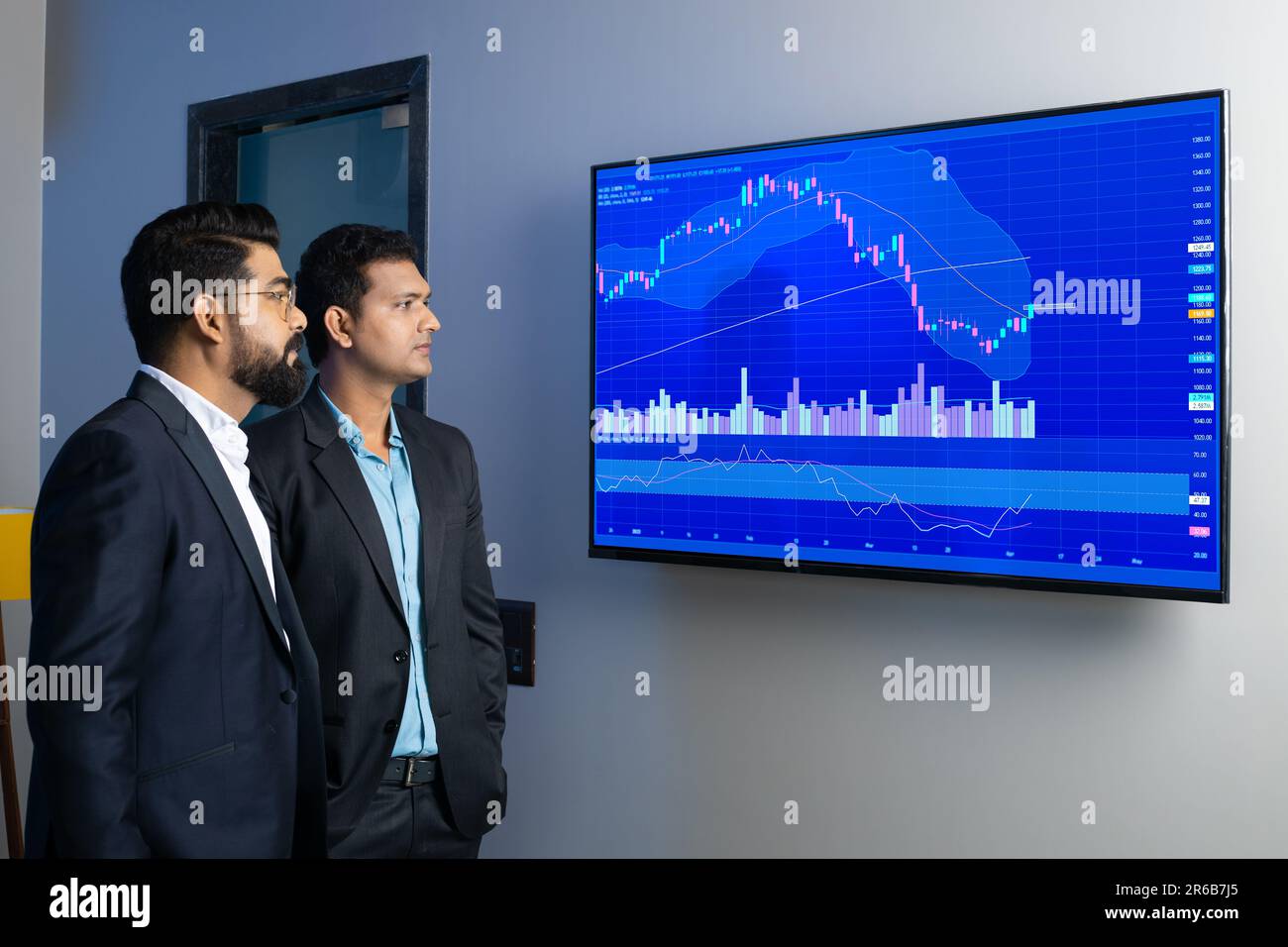 Des collègues d'hommes d'affaires indiens regardent des actions en ligne au bureau. Courtiers en Bourse regardant des graphiques d'index sur grand écran d'ordinateur. Marque financière commerciale Banque D'Images