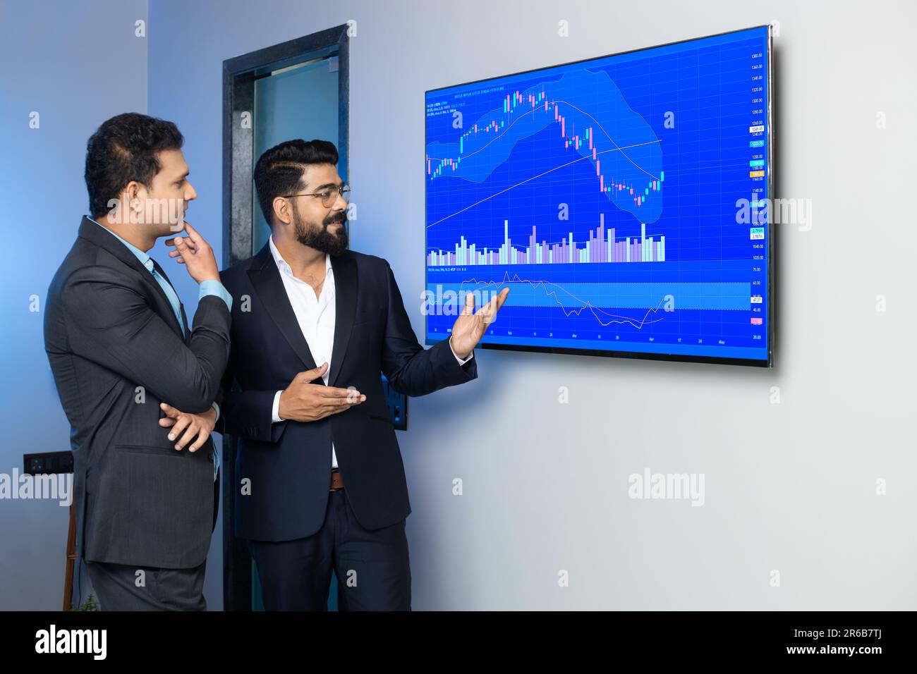 Des collègues d'hommes d'affaires indiens négociant et discutant des actions en ligne au bureau. Courtiers en Bourse regardant des graphiques d'index sur grand écran d'ordinateur. Banque D'Images