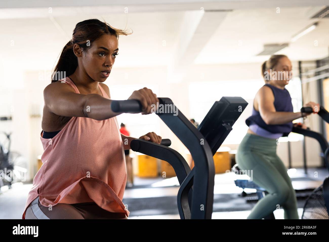 Confiante biracial jeune femme avec détermination s'exerçant sur machine elliptique d'entraînement dans la salle de gym Banque D'Images