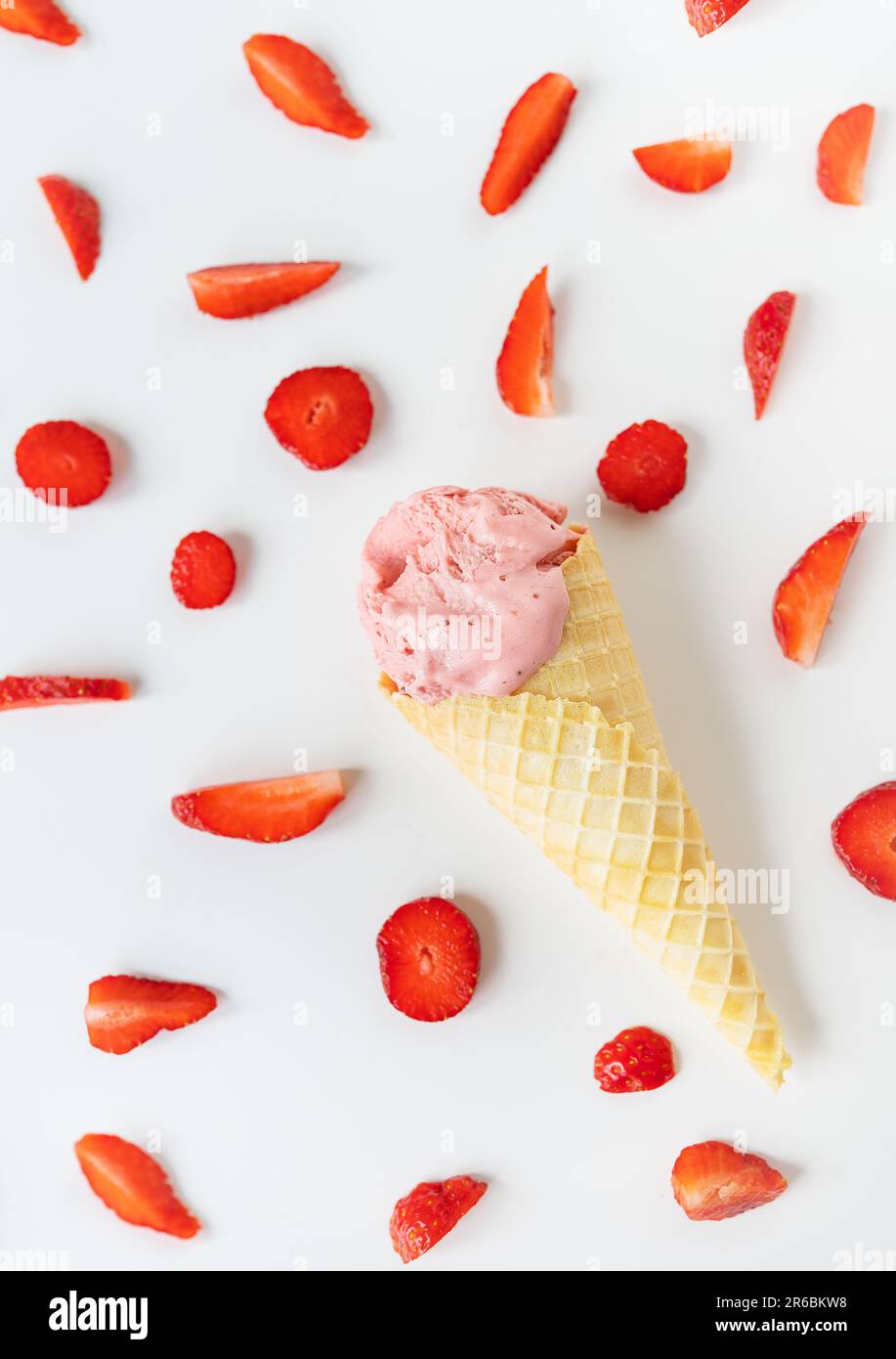 Crème glacée à la fraise dans une tasse à gaufres sous forme de cône, la crème glacée se trouve sur une table blanche avec des tranches de fraises fraîches. Photo verticale Banque D'Images