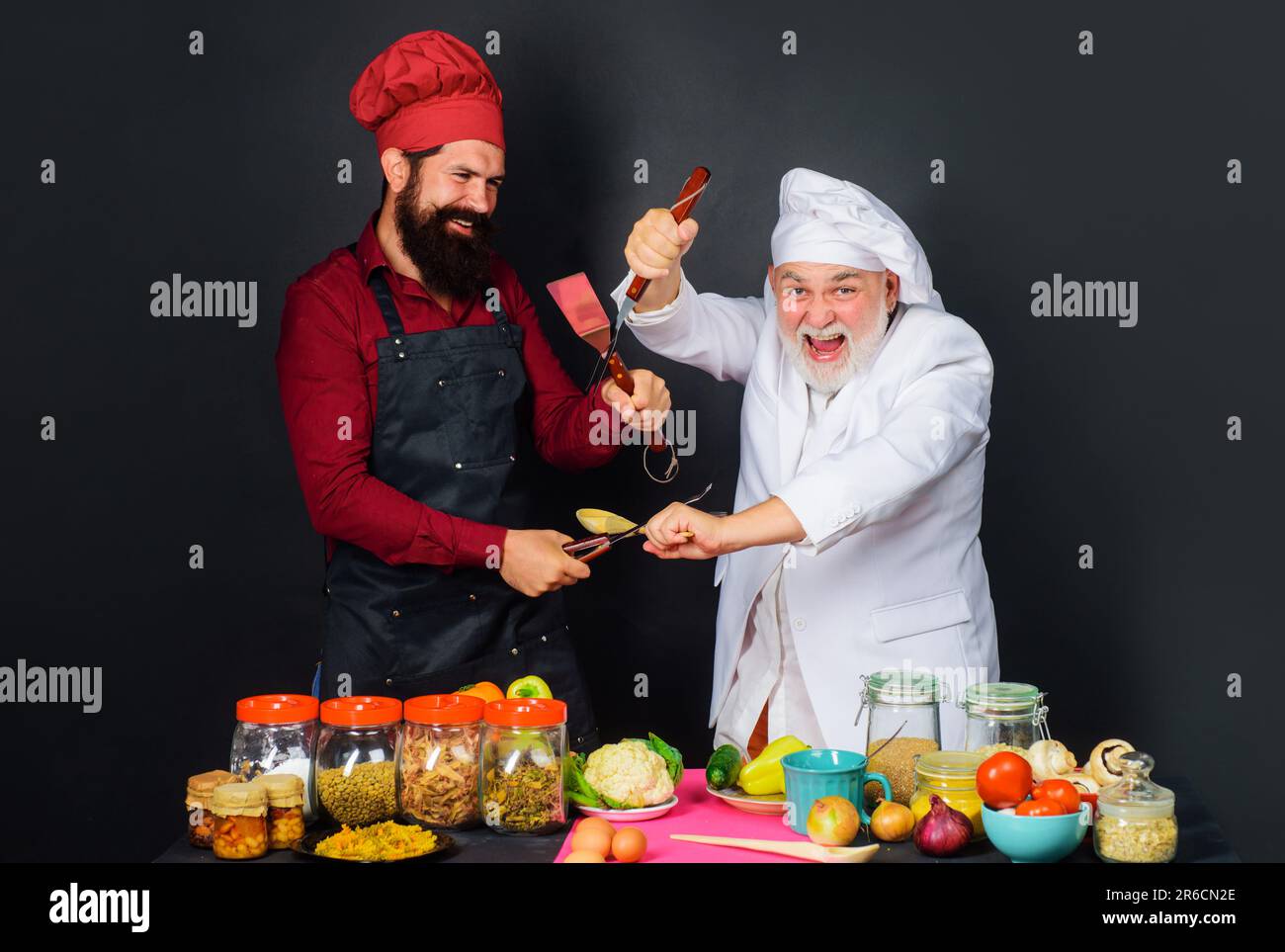 Deux chefs en uniforme se disputent dans la cuisine. Cuisine professionnelle. Règles de la cuisine. Défi de cuisine. Bataille culinaire dans la cuisine. Chefs barbus Banque D'Images