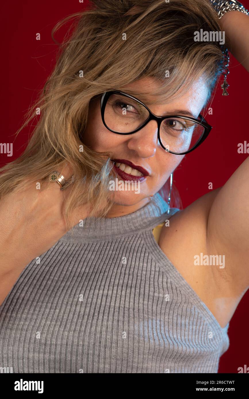 Portrait d'une belle femme blonde portant des lunettes souriant avec les mains dans les cheveux. Personne positive. Isolé sur fond rouge. Banque D'Images