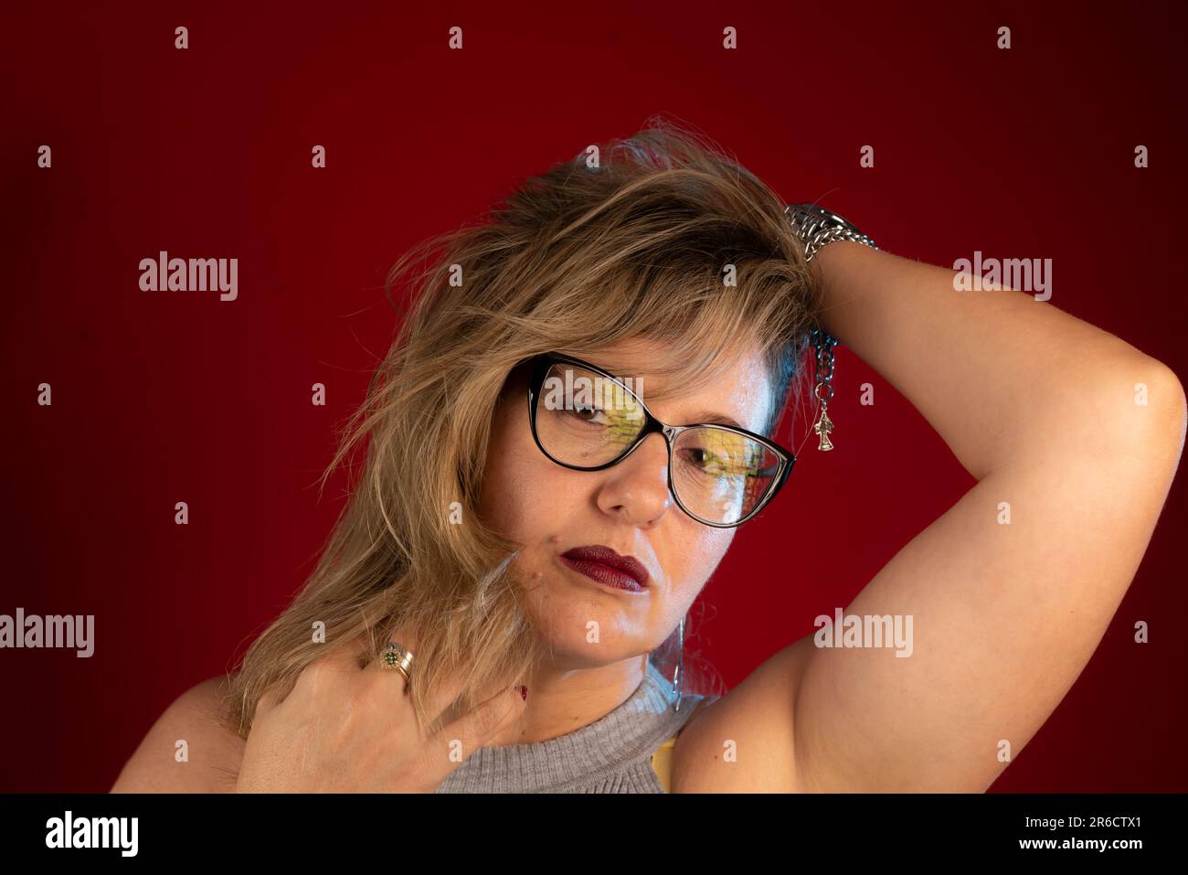 Portrait rapproché d'une belle femme mûre portant des lunettes avec les mains dans les cheveux. Personne positive. Isolé sur fond rouge. Banque D'Images