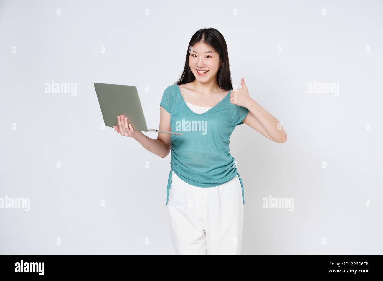 Jeune femme asiatique tenant un ordinateur portable et montrant les pouces isolés sur fond blanc. Banque D'Images