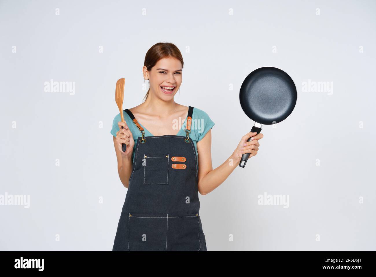 Jeune femme portant un tablier de cuisine avec un récipient et une spatule isolés sur fond blanc. Banque D'Images