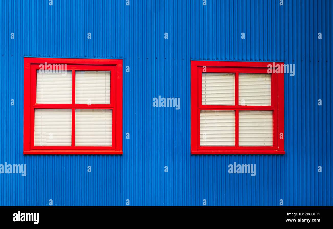 Deux fenêtres avec cadres en bois rouge dans un mur bleu. Extérieur d'une maison avec fenêtres et stores sont fermés. Belle façade de maison colorée. Personne Banque D'Images