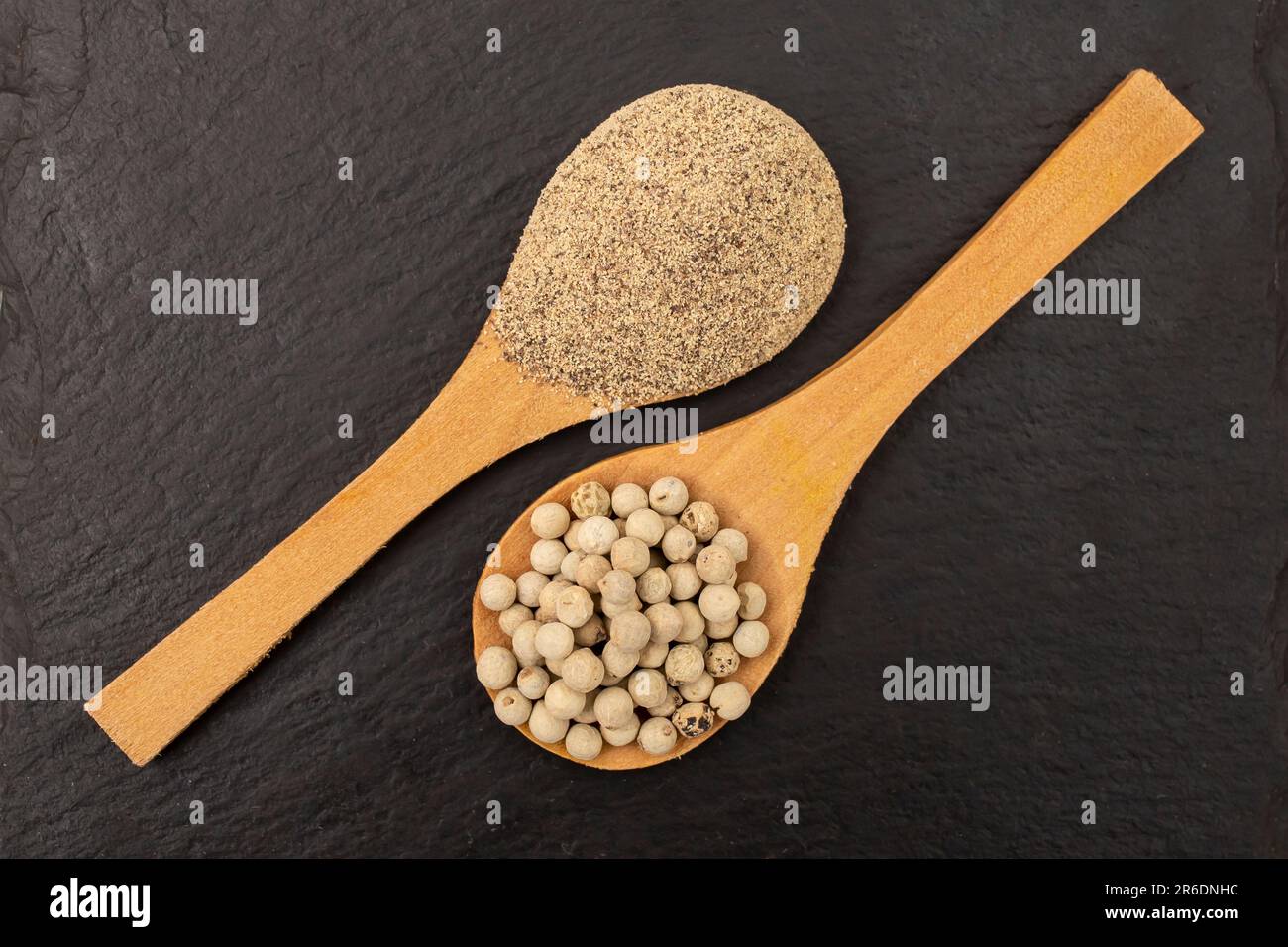 Graines de poivre blanc vs poudre et cuillères en bois, sur carreaux de pierre noire, plat de poser de près Banque D'Images