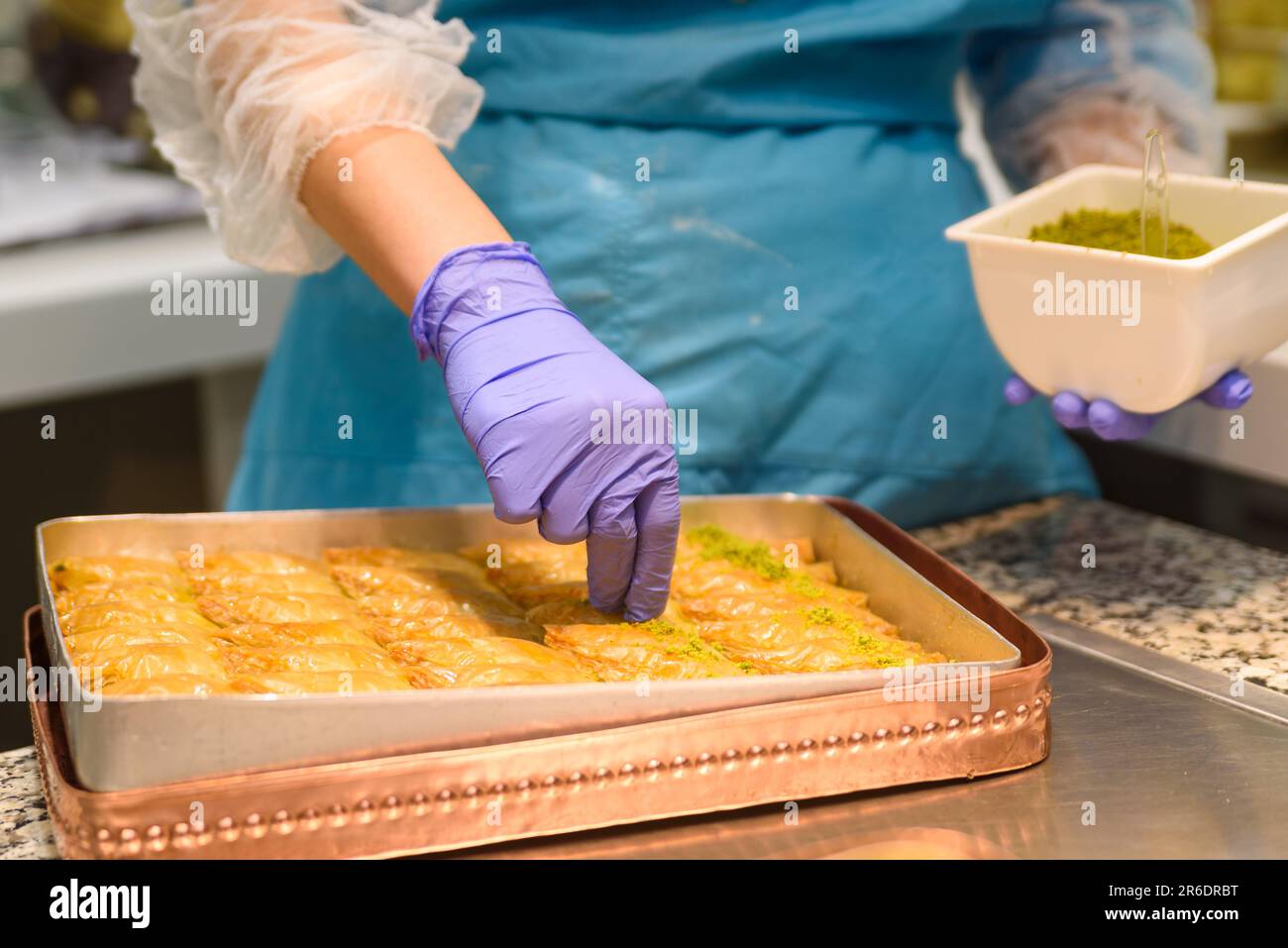 Gros plan des mains préparant des sucreries traditionnelles turques de baklava avec pistache à l'intérieur d'une boulangerie à Istanbul. Fabrication de baklava Banque D'Images