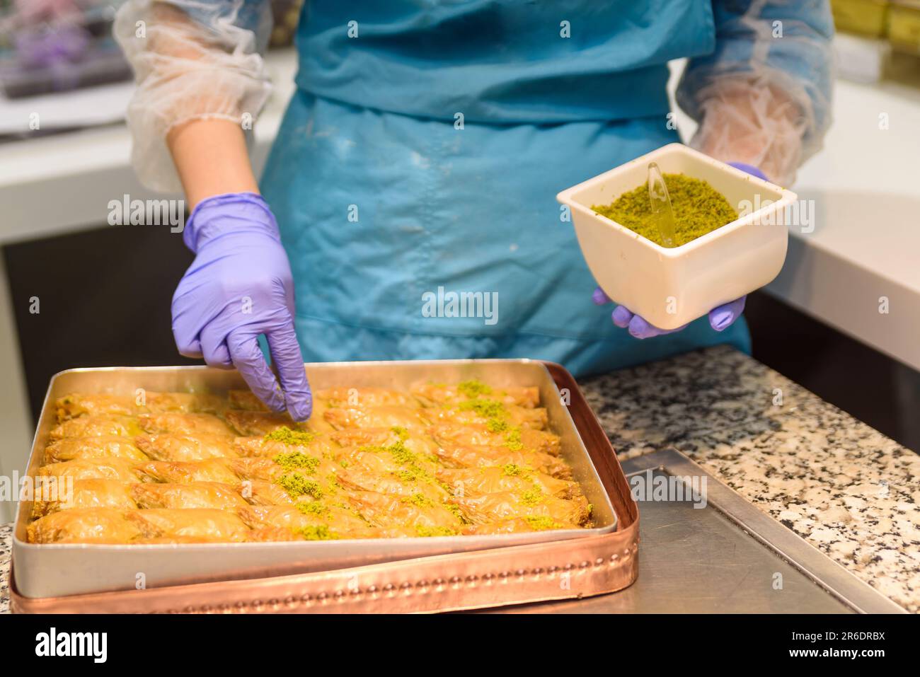 Gros plan des mains préparant des sucreries traditionnelles turques de baklava avec pistache à l'intérieur d'une boulangerie à Istanbul. Fabrication de baklava Banque D'Images