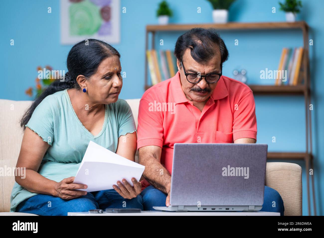 Couple indien senior discutant en vérifiant des documents ou des factures à l'aide d'un ordinateur portable à la maison - concept de technologie, planification financière et relation Banque D'Images