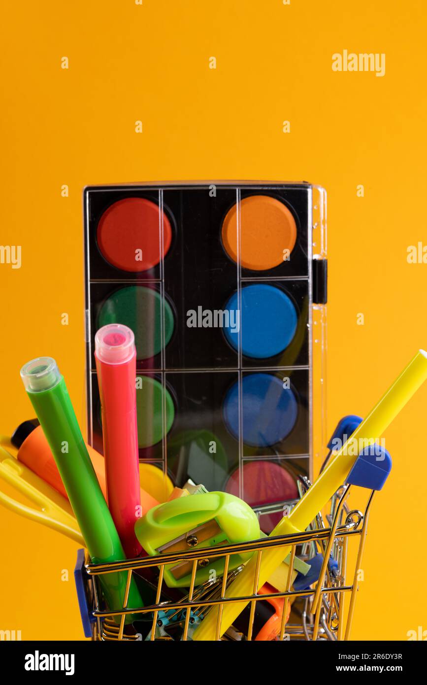 Gros plan sur un petit chariot de magasinage avec matériel scolaire et espace de copie sur fond orange. Retour à l'école, shopping, matériel scolaire, apprentissage Banque D'Images