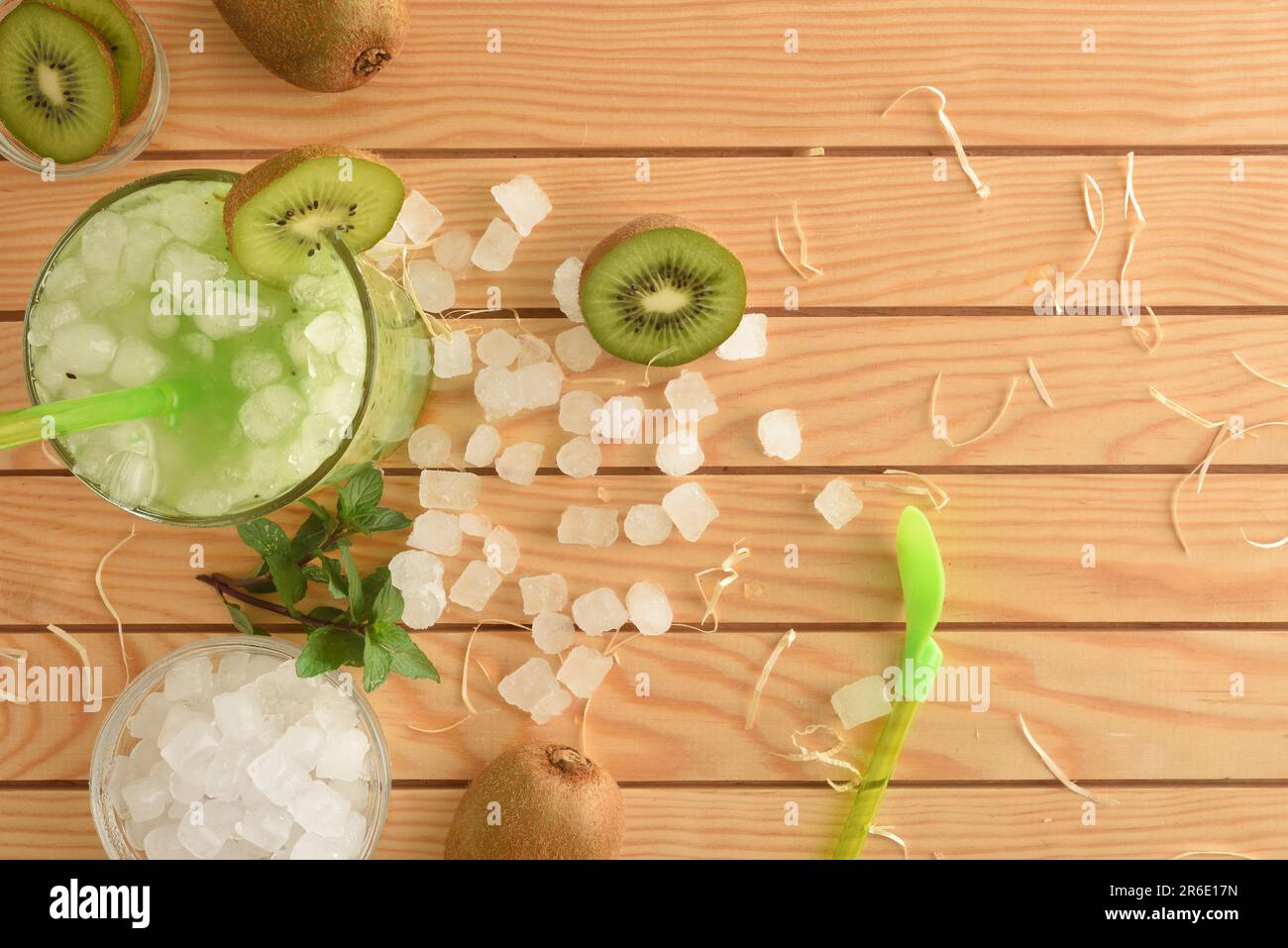 Détail d'un verre avec jus de kiwi et glace sur une table en bois avec des fruits et de la glace pilée autour. Vue de dessus. Composition horizontale. Banque D'Images
