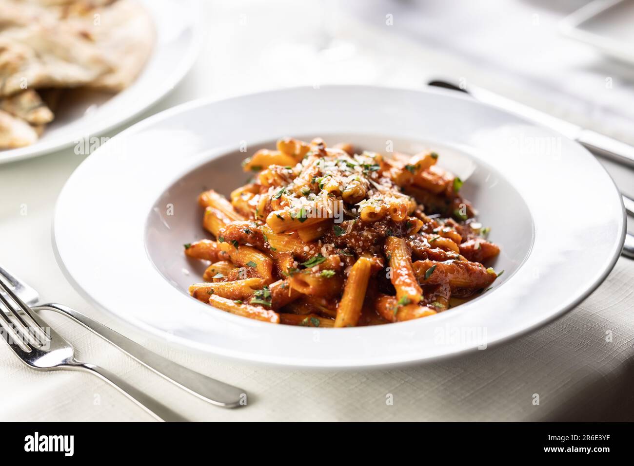Pène alla arrabiata, pâtes à la sauce rouge italienne servies sur une table dans une assiette avec une râpe fraîche de parmesan. Banque D'Images