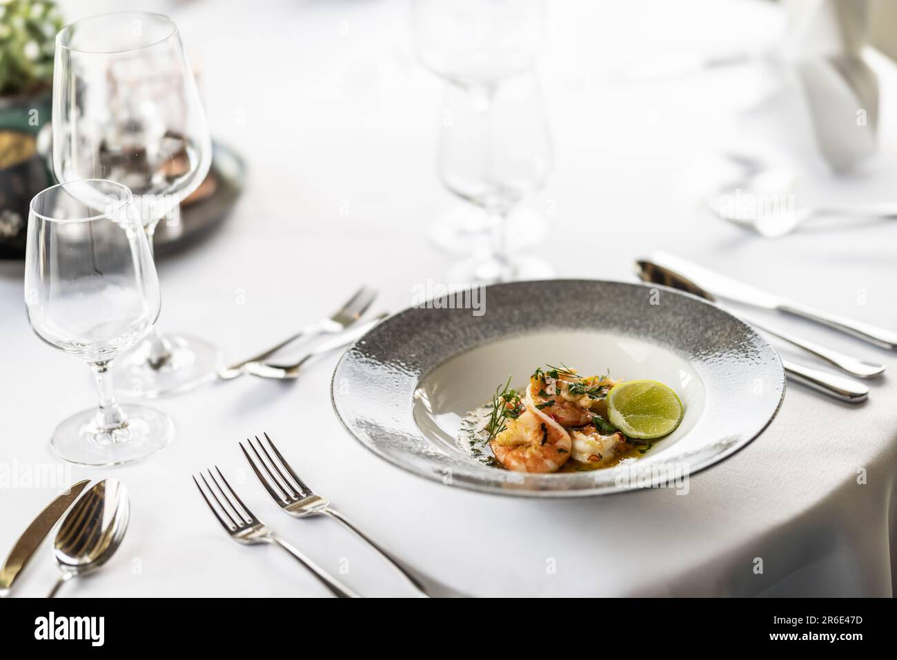 Décor blanc d'une table formelle dans un restaurant avec une assiette de hors-d'œuvre sous forme de piment grillé et de crevettes à l'ail. Banque D'Images