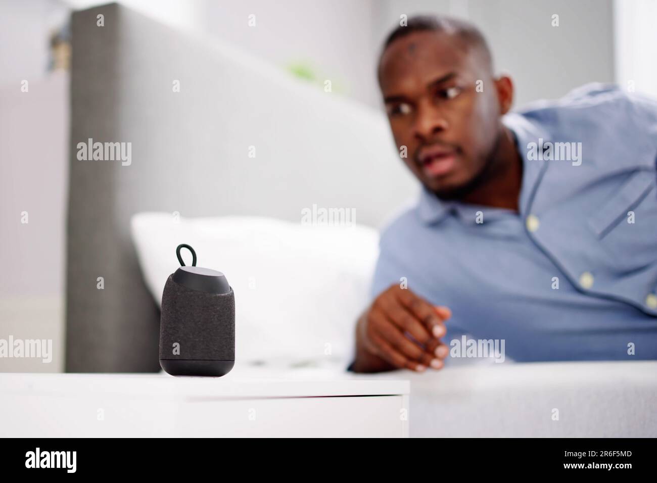 Jeune homme souriant couché sur le lit écouter de la musique sur le haut-parleur sans fil Banque D'Images