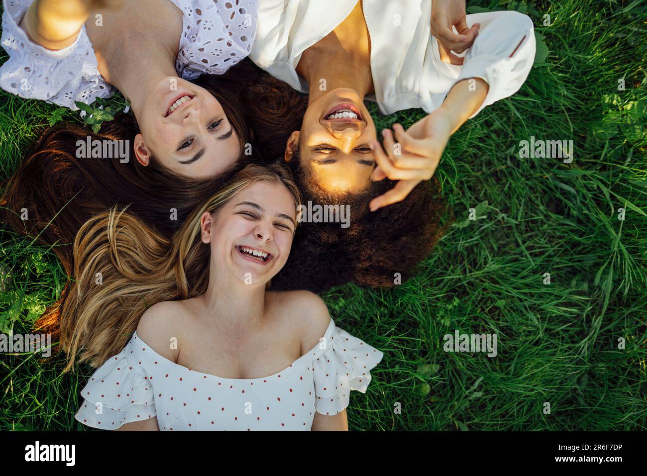 Trois jeunes femmes adorables de différentes origines ethniques dans des robes blanches élégantes sont sur l'herbe. Les filles souriantes ont passé un excellent moment ensemble sur la prairie. Caucas amusants Banque D'Images