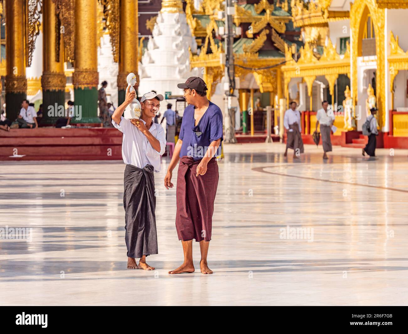 Deux hommes parlent, dont un portant une image de Bouddha sur son épaule, à la Pagode Shwedagon à Yangon, au Myanmar. Banque D'Images
