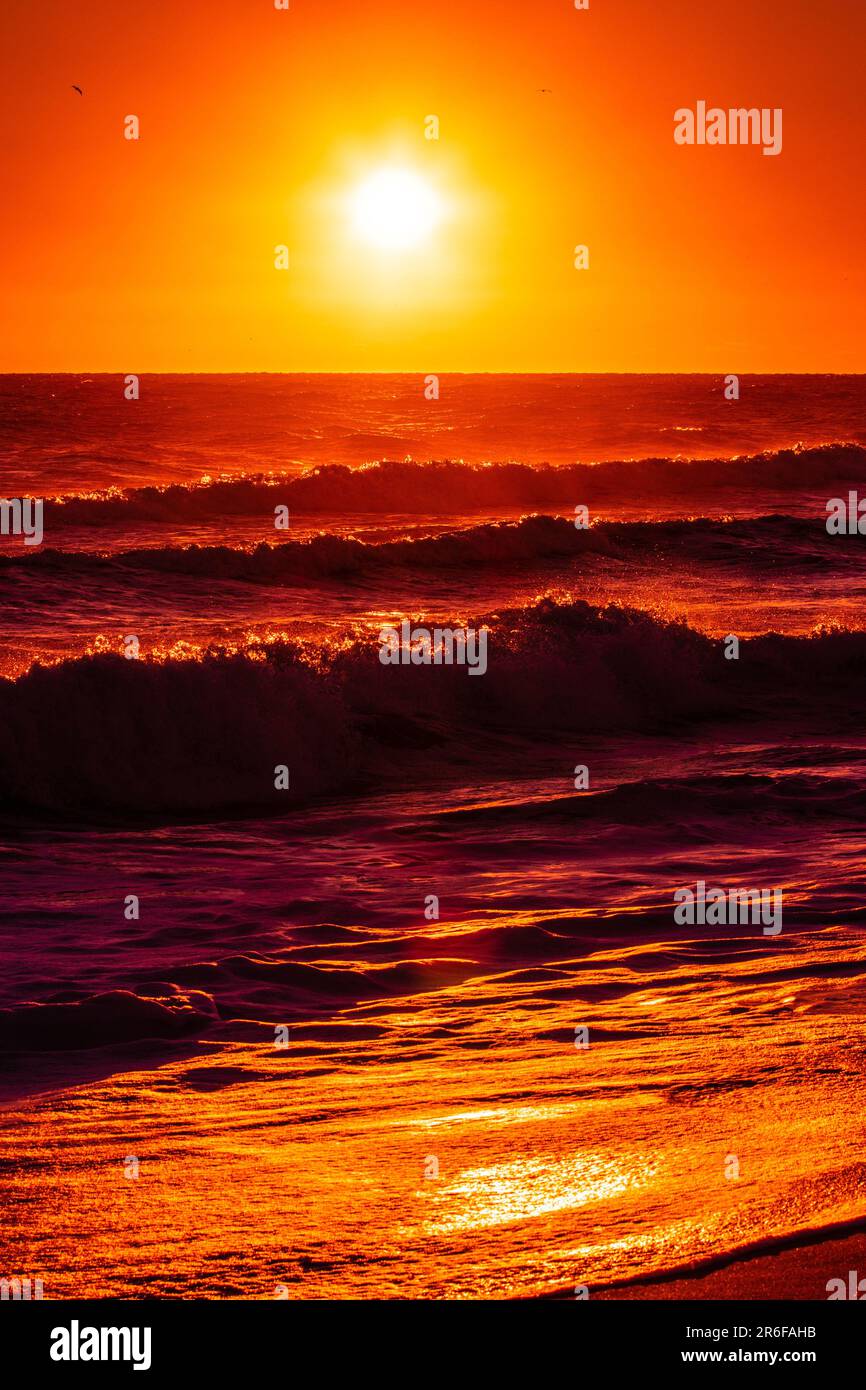 Un majestueux coucher de soleil rouge et orange sur un océan paisible avec des vagues paisibles Banque D'Images
