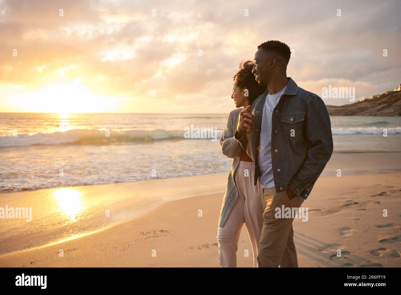 Jeune couple multiethnique souriant regardant le coucher de soleil sur une plage Banque D'Images