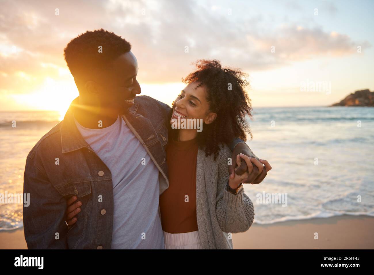 Couple multiethnique souriant debout ensemble sur une plage de sable au crépuscule Banque D'Images