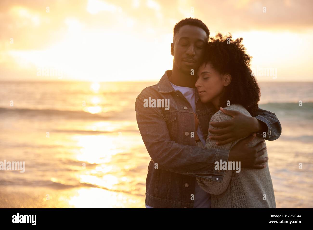 Jeune couple multiethnique aimant se tenant sur une plage au coucher du soleil Banque D'Images