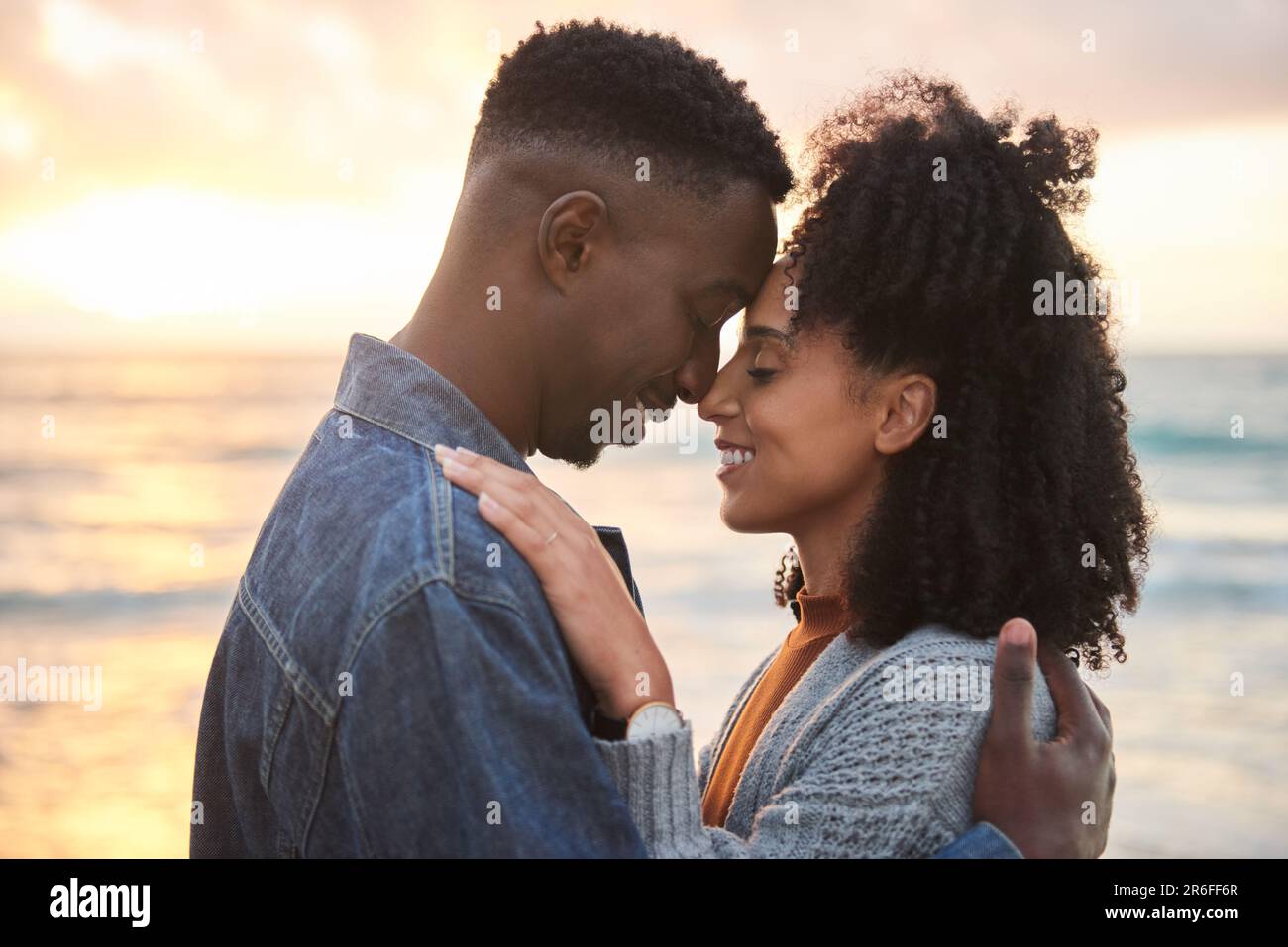 Couple multiethnique aimant avec les yeux fermés debout sur une plage au crépuscule Banque D'Images