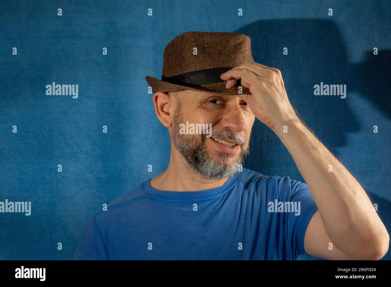 Un homme portant un t-shirt bleu et un chapeau debout contre un mur bleu avec une expression sérieuse Banque D'Images