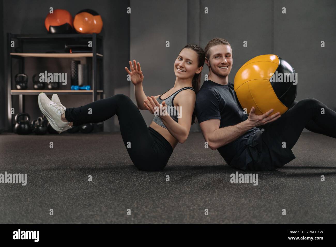 Bonne tenue d'entraînement de couple crossfit ensemble à la salle de gym  sombre avec équipement de sport professionnel sur fond. Faites de  l'exercice abs à l'aide d'un ballon de médecine et faites-le