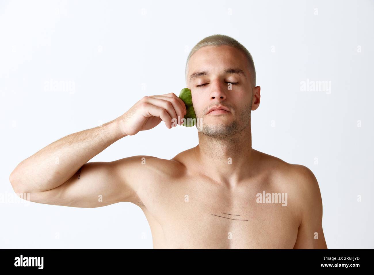 Soulèvement du visage, soin anti-rides. Jeune homme beau faisant un massage du visage avec un outil cosmétologique sur fond blanc de studio Banque D'Images