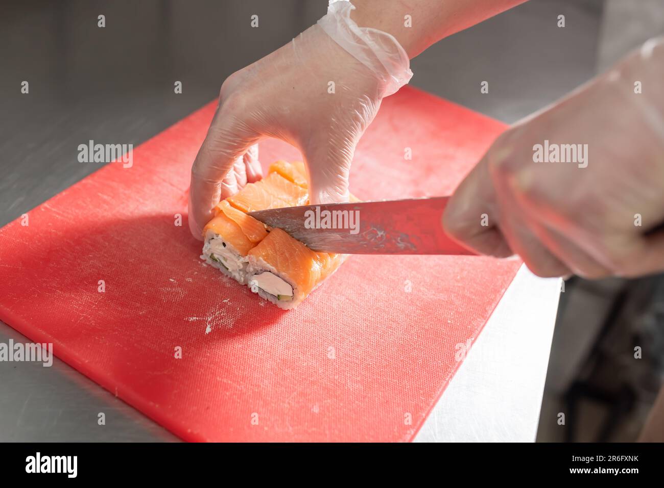 Le cuisinier coupe des sushis roulés de saumon, de fromage et de concombre sur un plateau rouge. Photo de haute qualité Banque D'Images