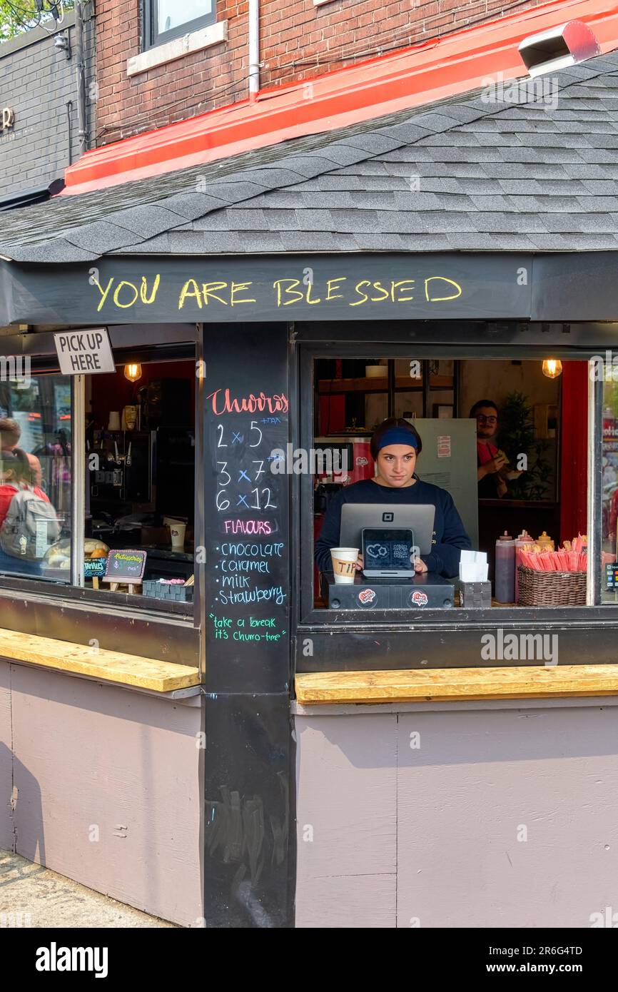 Toronto, Canada - 4 juin 2023 : marché de Kensington. Une jeune femme qui travaille comme caissière dans une cafétéria. L'extérieur du magasin porte l'inscription « Yo Banque D'Images