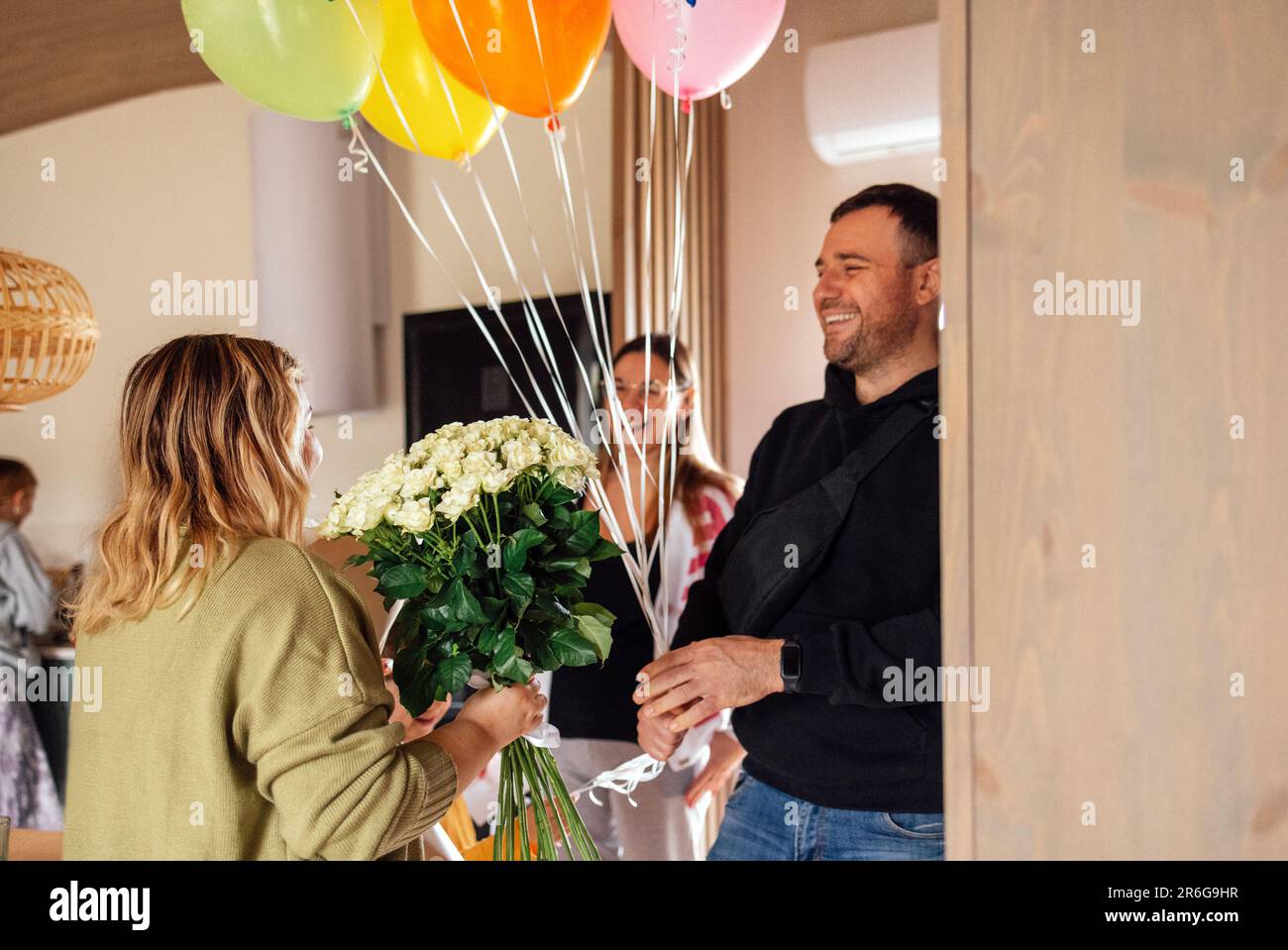 Un jeune couple félicite la blonde féminine de son anniversaire. Belle femme en verres donne un bouquet de fleurs blanches et baisers anniversaire fille. Mains Banque D'Images