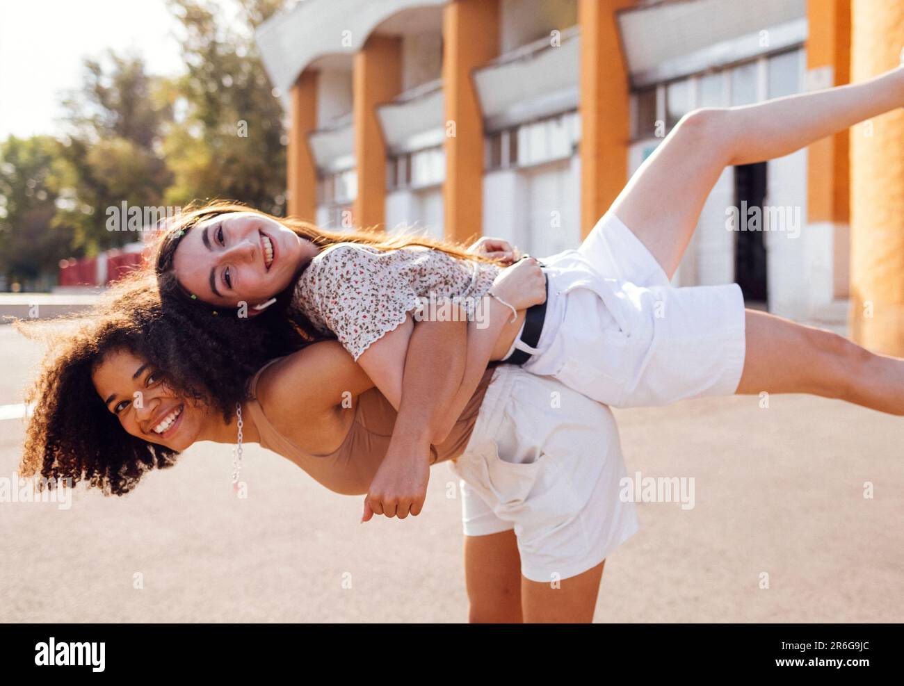 Deux adolescentes multiraciales qui s'embrasent et s'amusent ensemble. Des amis heureux dans des vêtements décontractés qui se moque et rient dans la rue urbaine. Joli gir Banque D'Images