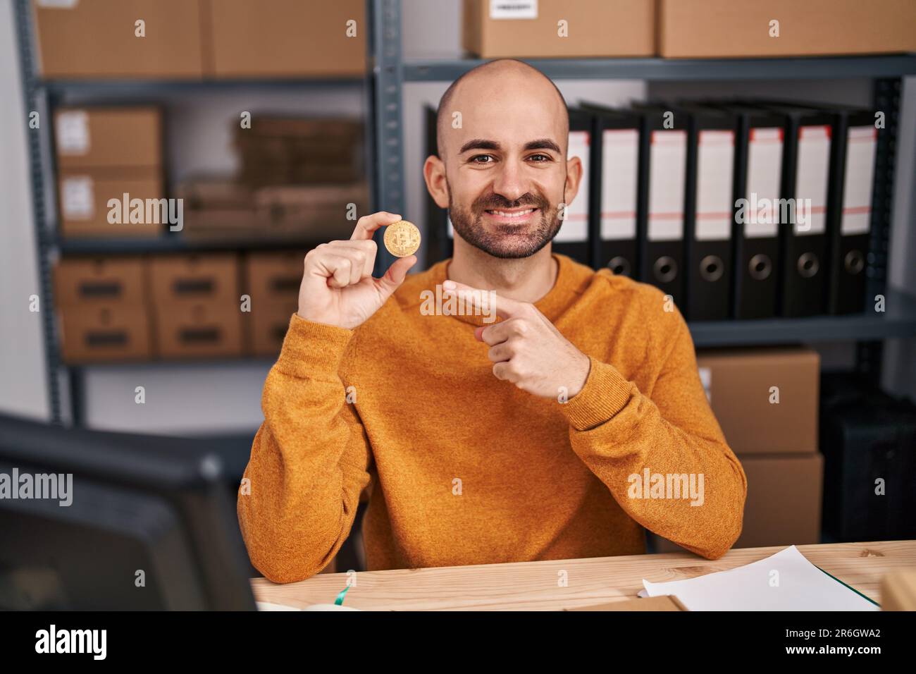 Jeune homme chauve avec la barbe de travail à la petite entreprise ecommerce tenant bitcoin sourire heureux pointant avec la main et le doigt Banque D'Images