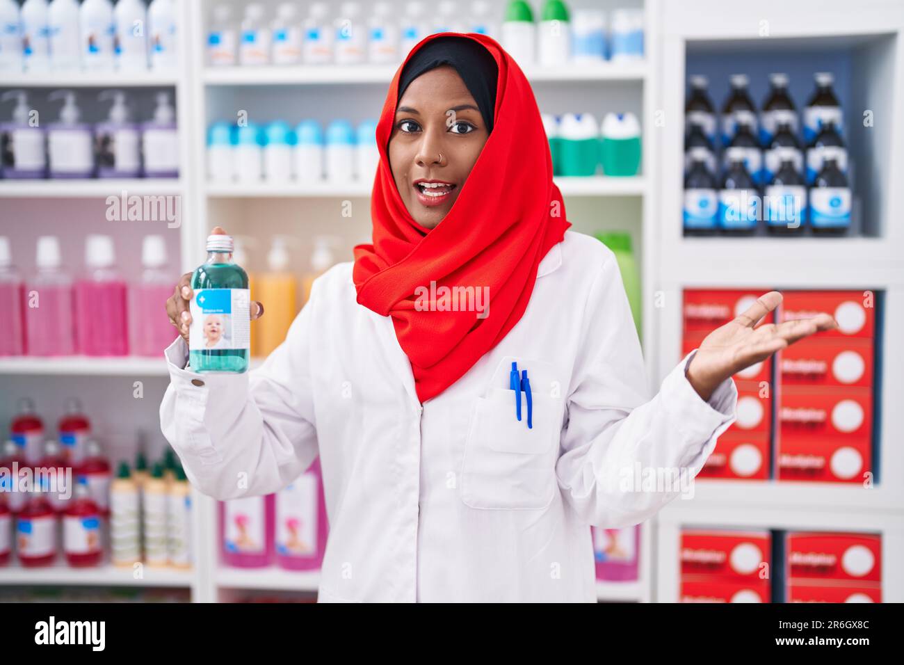 Jeune femme arabe travaillant à la pharmacie pharmacie pharmacie de pharmacie holding sirop célébrant la réalisation avec le sourire heureux et l'expression de gagnant avec la main levée Banque D'Images