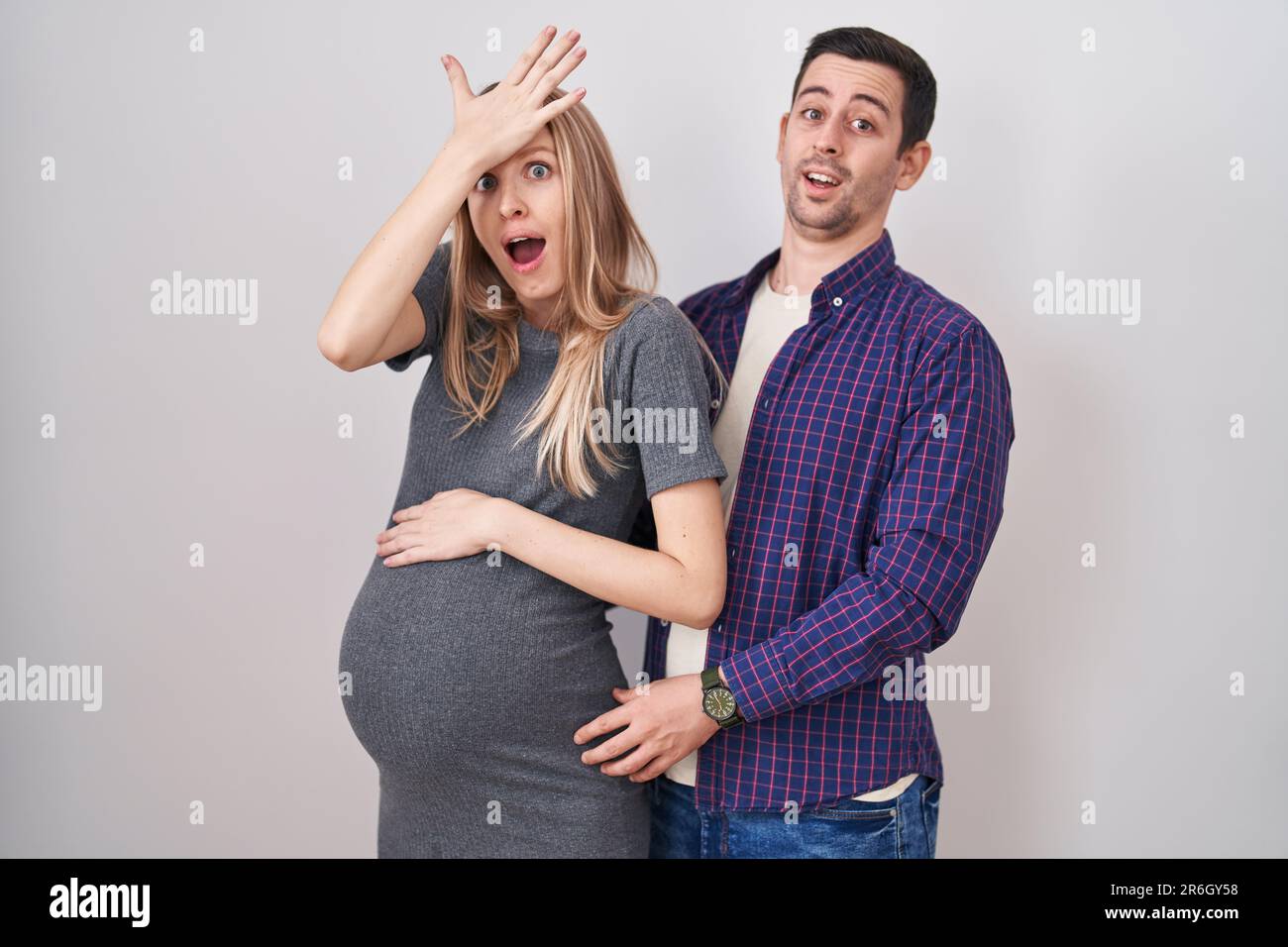 Jeune couple s'attendant à un bébé debout sur fond blanc surpris par la main sur la tête pour erreur, rappelez-vous erreur. oubli, mauvais concept de mémoire. Banque D'Images Jeune couple s'attendant à un bébé debout sur fond blanc surpris par la main sur la tête pour erreur, rappelez-vous erreur. oubli, mauvais concept de mémoire. Banque D'Images