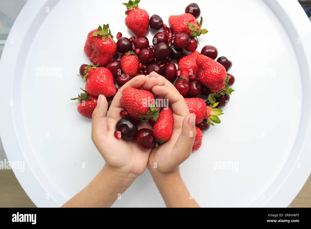 Table blanche avec fraises et cerises fraîches, mains des filles Banque D'Images