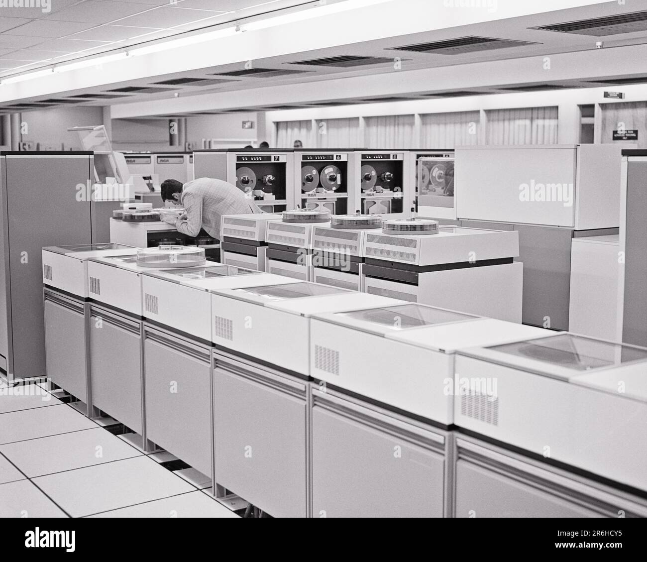 1960S HOMME ANONYME TECHNICIEN DANS UNE GRANDE SALLE INFORMATIQUE MAINFRAME METTANT DES DISQUES DE STOCKAGE SUR PLATEAU AMOVIBLES DANS L'UN DES PLUSIEURS LECTEURS - O2753 HAR001 HARS PERSONNES TECHNICIEN HOMMES PROFESSION B&W TRAITEMENT COMPÉTENCES MÉTIER MAINFRAME GRAND ANGLE CARRIÈRES ÉLECTRONIQUE SAVOIR PUISSANT INDÉPENDANT MÉTIERS DE L'INNOVATION HIGH TECH CONCEPT SÉPARÉ SOLITAIRE ANONYME SOLO HAUTE VITESSE BOBINE À BOBINE JEUNE HOMME ADULTE NOIR ET BLANC CAUCASIENS CALCUL DE L'ETHNICITÉ HAR001 INDIVIDU VIEUX MODE Banque D'Images