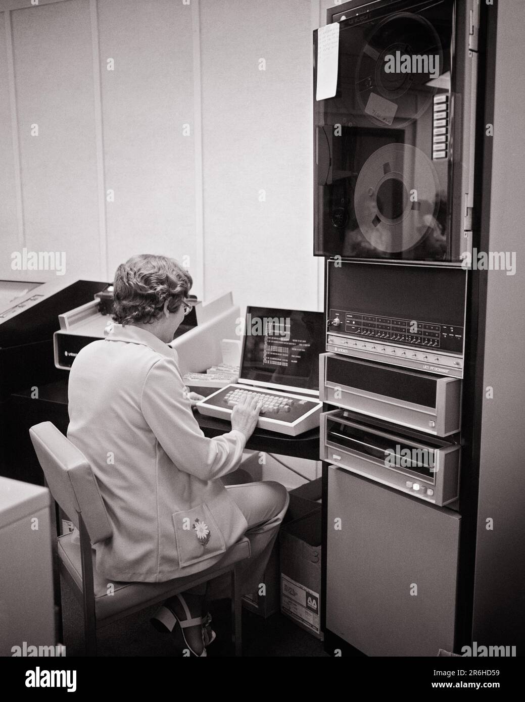 1970S VUE ARRIÈRE D'UNE FEMME QUI TRAVAILLE SUR UN POSTE DE TRAVAIL D'ORDINATEUR À CÔTÉ D'UNE COLONNE DE STOCKAGE DE BOBINE À BOBINE - O4229 HAR001 HARS COMPÉTENCES RÉSEAUTAGE COLONNE ÉLECTRONIQUE INNOVATION MAIN-D'ŒUVRE ARRIÈRE VUE EMPLOI PROFESSIONS HAUTE TECHNOLOGIE SAISIE DE DONNÉES DE DERRIÈRE LE MONITEUR VUE ARRIÈRE DE L'EMPLOYÉ MOYENNE-ADULTE MOYENNE-ADULTE DE LA BOBINE DE LA FEMME NOIR ET BLANC DE RACE BLANCHE DE CALCUL HAR001 TRAVAIL À L'ANCIENNE STATION DE TRAVAIL Banque D'Images