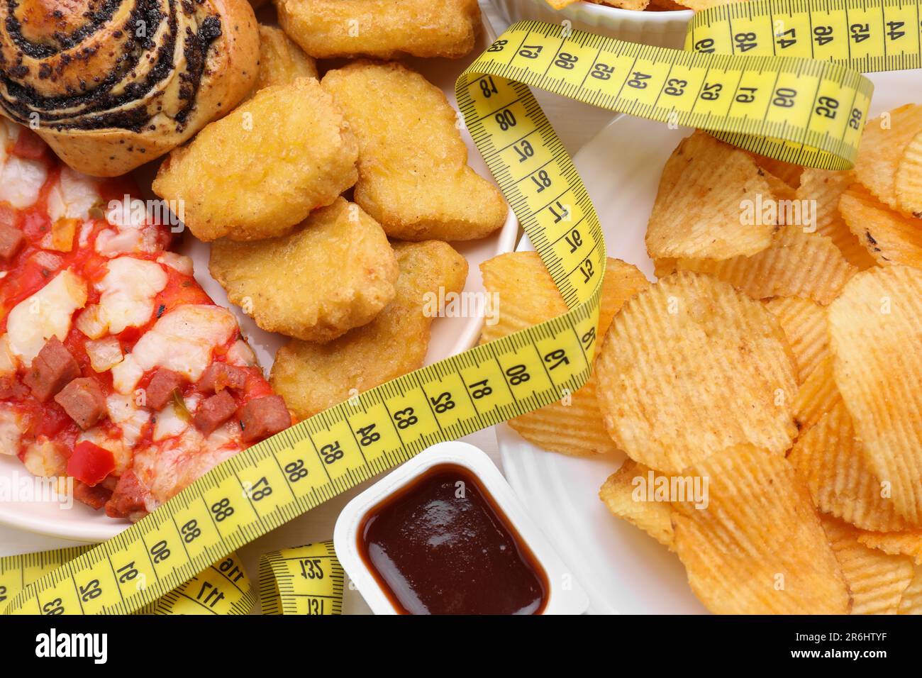 Différents aliments malsains et mètre ruban sur table blanche, vue de dessus. Concept de perte de poids Banque D'Images