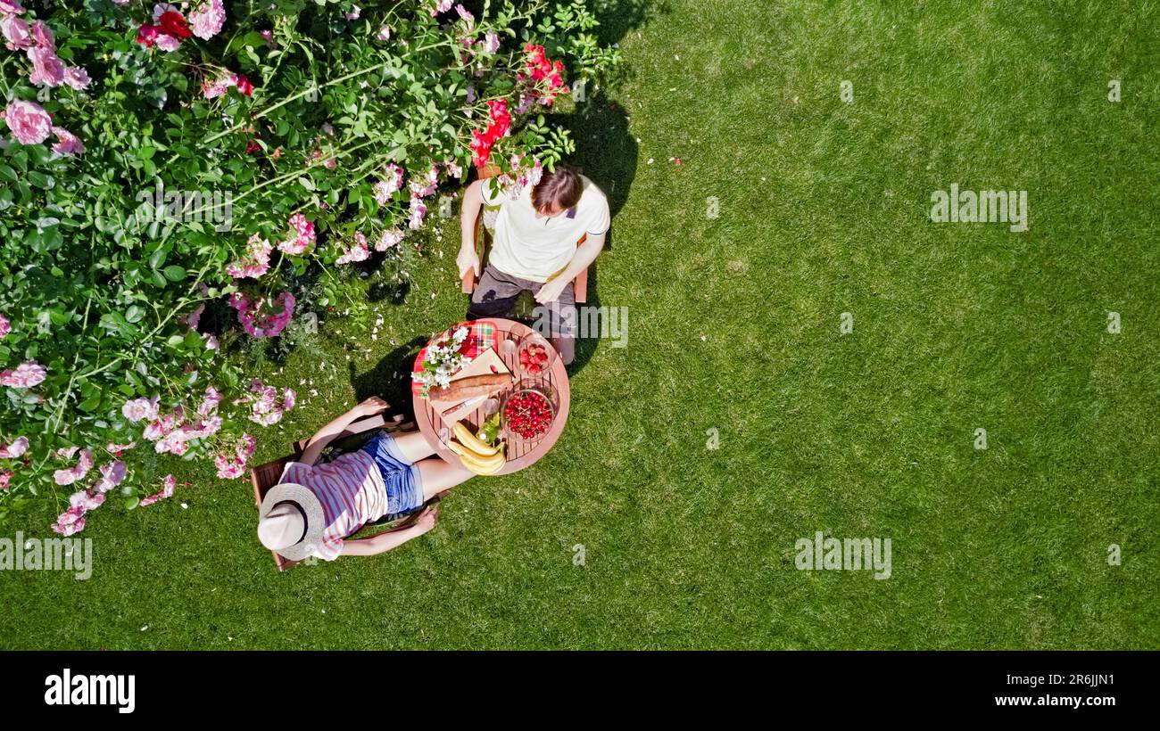 Jeune couple appréciant la nourriture et les boissons dans le magnifique jardin de roses à la date romantique, vue aérienne de dessus de l'homme et la femme manger et boire Banque D'Images