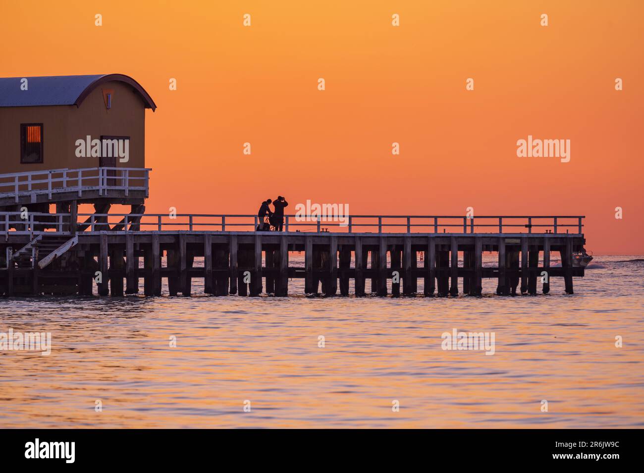 Silhouette d'un couple sur une jetée côtière contre un ciel doré à l'aube à Queenscliff à Victoria, en Australie Banque D'Images