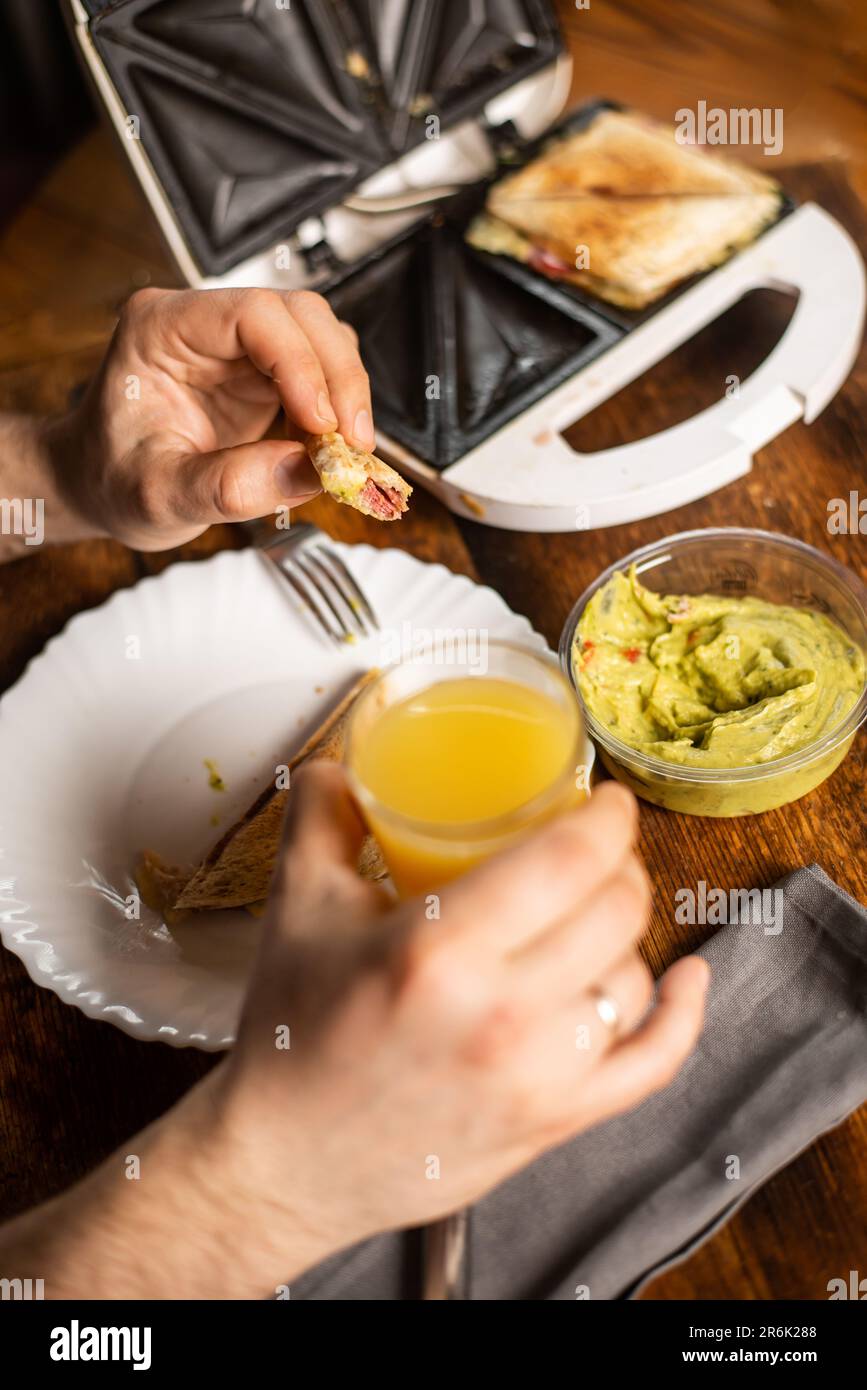 Heure du petit déjeuner. Homme méconnaissable tenant un verre de jus d'orange. Le sandwich se trouve sur l'assiette. Banque D'Images