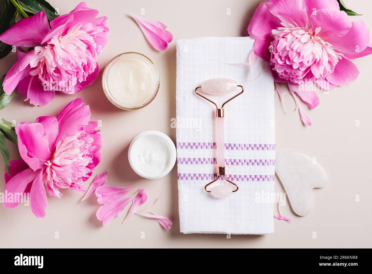 Crèmes roulaines et faciales sur fond rose avec pivoines, soins du visage et du cou, soins spa. Banque D'Images